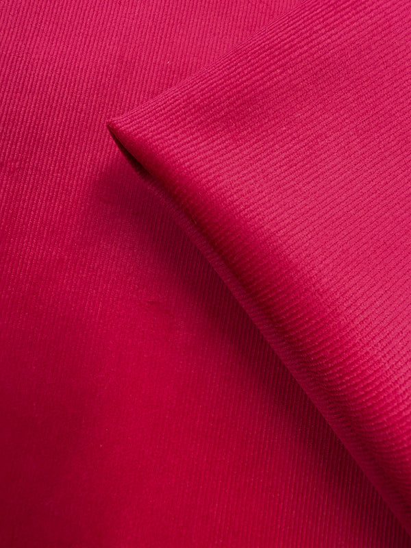 A close-up of Super Cheap Fabrics’ Pin Wale Corduroy - Love Potion (147cm), showing its bright pink color, fine ribbed texture, and smooth, medium weight cotton fabric with a neatly folded corner.