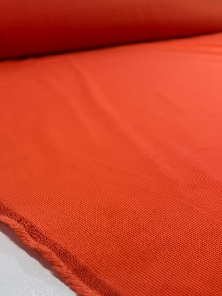A close-up of Super Cheap Fabrics' Pin Wale Corduroy - Fiesta (142cm) in bright orange, highlighting its smooth texture and subtle ribbed edge, displayed flat on a white surface.