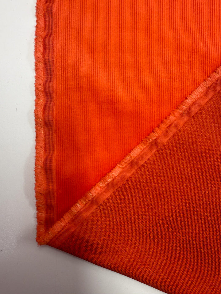 A close-up of two overlapping Pin Wale Corduroy - Fiesta - 142cm fabric pieces by Super Cheap Fabrics, showing textured edges and visible weave patterns arranged diagonally on a white surface.