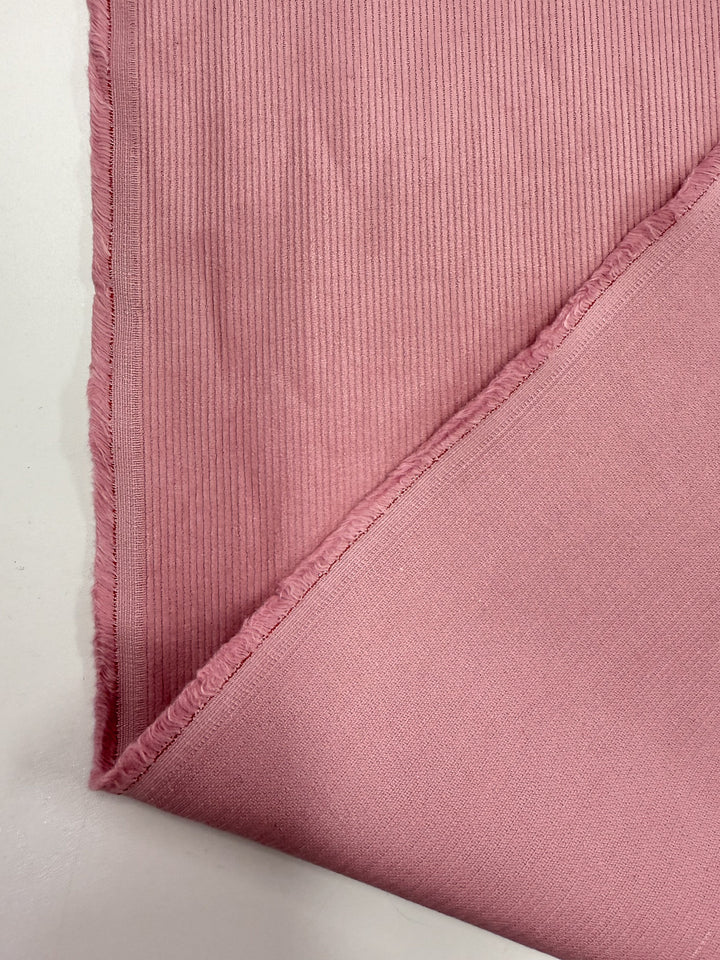 A close-up of Super Cheap Fabrics' Pin Wale Corduroy - Blush (147cm), folded at the corner to showcase its soft ribbed texture and smooth backing—ideal for creating cozy winter clothing.