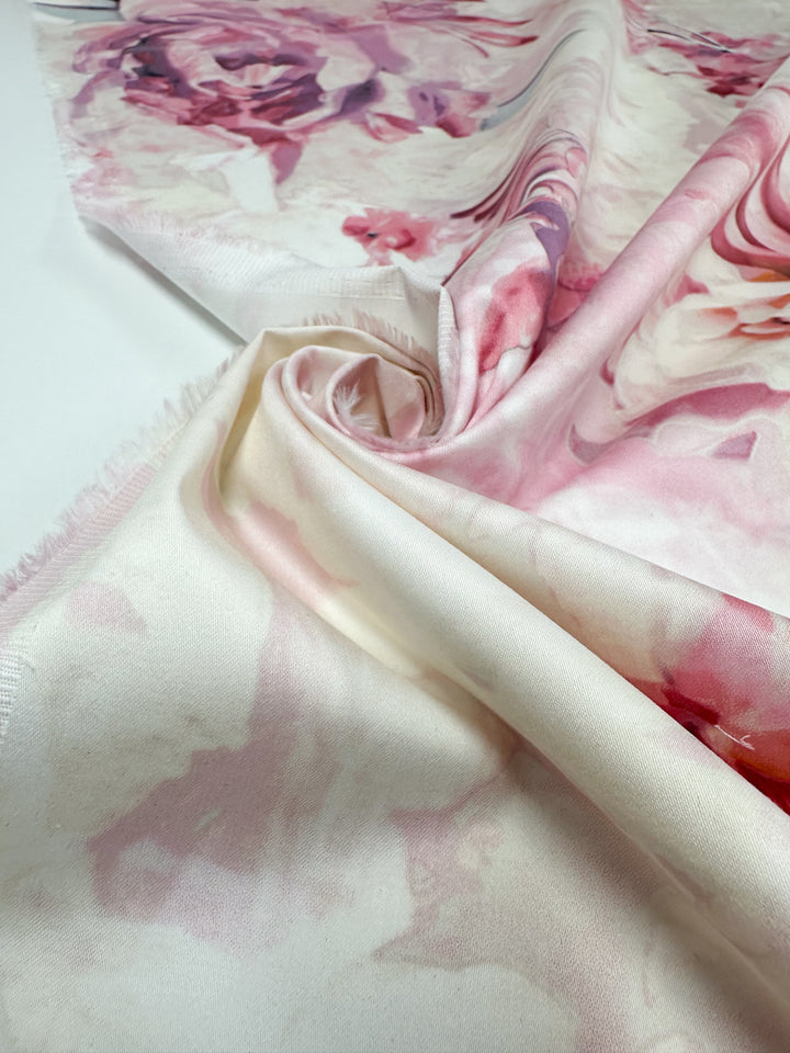 A close-up of Super Cheap Fabrics' Cotton Sateen - Mystic Garden - 125cm showcases a flowing medium-weight fabric with a floral pattern in soft pink and white tones, perfect for household décor. The draped and partially rolled cotton reveals its smooth texture and delicate design.