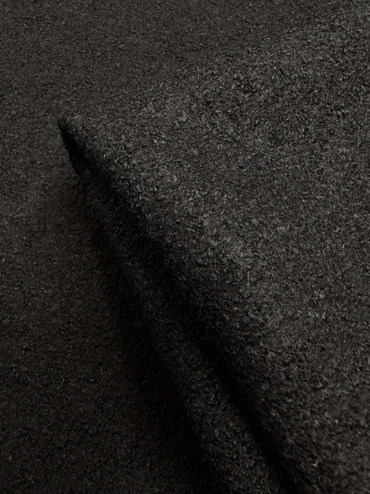 Close-up of Super Cheap Fabrics' Boiled Wool - Black - 145cm, showing its dark, textured appearance. The folded material highlights its thick and dense weave, with lighting emphasizing its rich color.