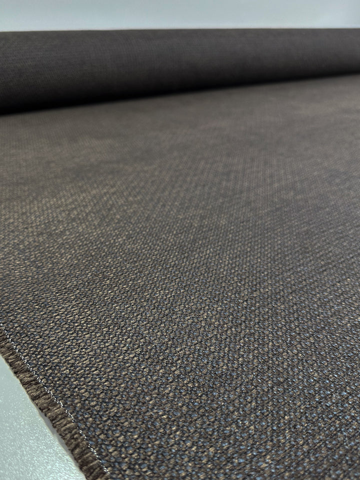 A close-up of Super Cheap Fabrics' Basket Weave Upholstery - Tuco 035 - 147cm shows coarse, tightly woven patterns. This durable fabric unrolls across a surface, extending into the distance with the roll partly visible at the top.