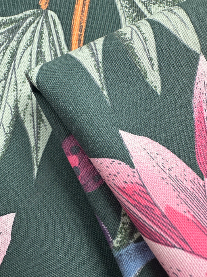 Close-up of folded Super Cheap Fabrics' Cotton Duck - Tropical Punch, perfect for home décor. This medium weight fabric showcases large green leaves and pink flowers on a dark green background, revealing intricate leaf and petal detailing with its visible texture. Width: 147cm.