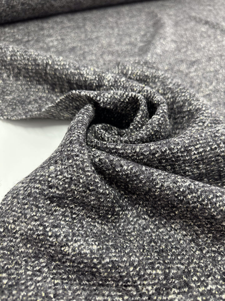A close-up of Super Cheap Fabrics' Boiled Wool - Lamé Charcoal Marle reveals a textured heavy weight fabric skillfully gathered into a swirl pattern, with its intricate weave and speckled appearance offering a rich, tactile surface.