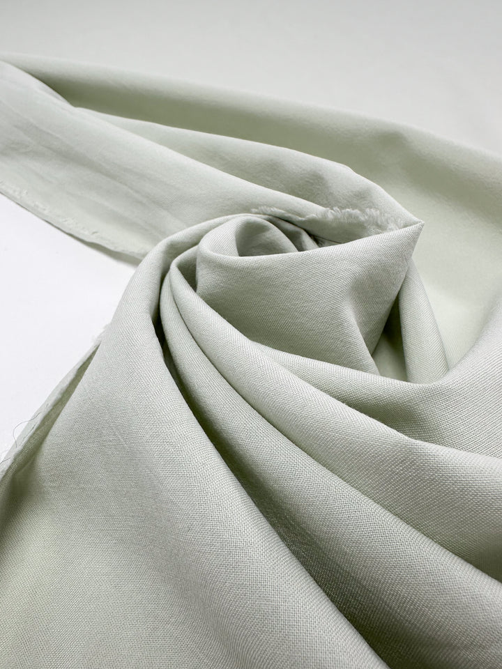 A close-up of Super Cheap Fabrics' 152cm Plain Cotton in Fairest Jade shows it elegantly spiraled. This lightweight fabric has a soft texture and subtle sheen, creating gentle shadows and highlights on its surface.