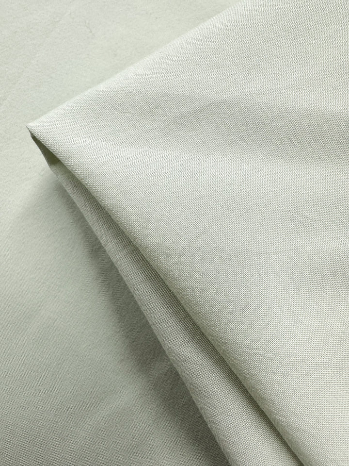 A close-up shows a neatly folded light gray fabric with fine, even weaves and a smooth texture. The lightweight cotton from Super Cheap Fabrics, named "Fairest Jade," is 152cm wide with a soft, matte finish.