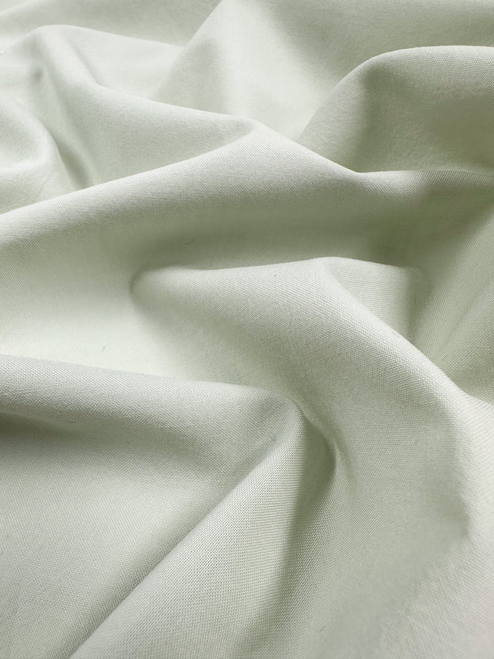 The Fairest Jade Plain Cotton by Super Cheap Fabrics, measuring 152cm, features a soft and crumpled texture with gentle folds. The light plays on its subtle curves and shadows, highlighting its lightweight nature and evoking fluidity and softness.
