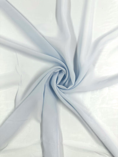 The Hi-Multi Chiffon - Skywriting - 150cm by Super Cheap Fabrics features a soft, light blue polyester fabric exquisitely gathered at the center to form a spiral pattern, with its lightweight and smooth texture creating delicate, outward radiating folds.