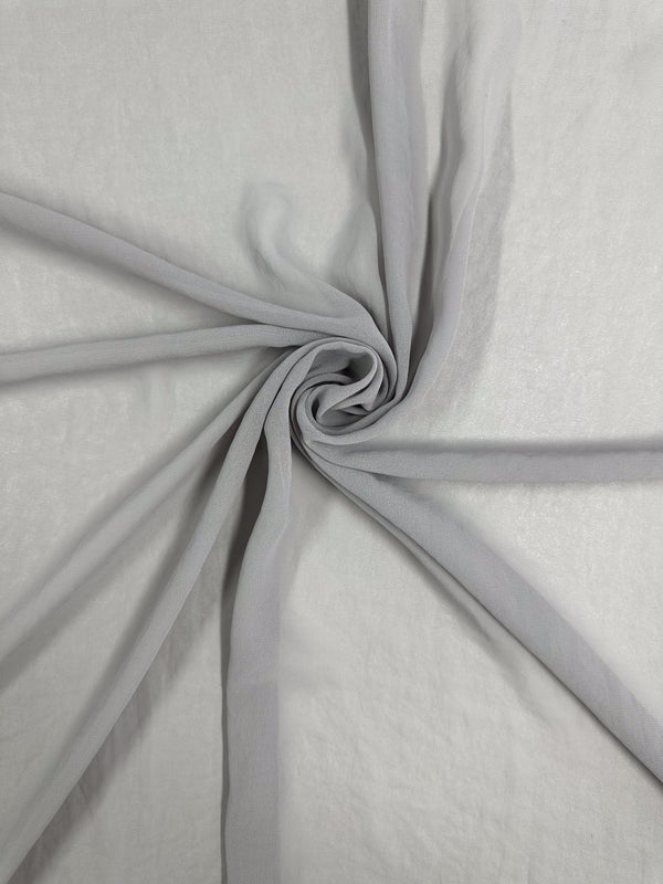 The Hi-Multi Chiffon - Harbor Mist by Super Cheap Fabrics features sheer gray fabric twisted into a spiral, forming a star-like pattern with soft folds extending outward on a flat surface.