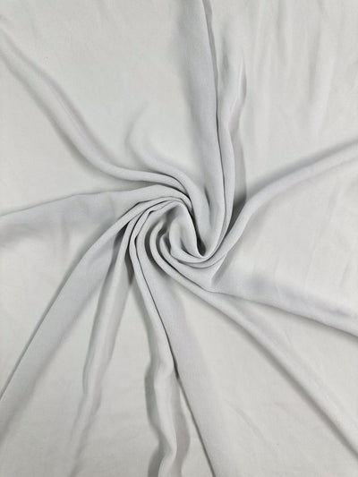 The Hi-Multi Chiffon - Oyster Mushroom from Super Cheap Fabrics is a light gray, lightweight fabric twisted into a spiral pattern, creating gathered folds that accentuate its soft, smooth texture—ideal for crafting floaty tops.