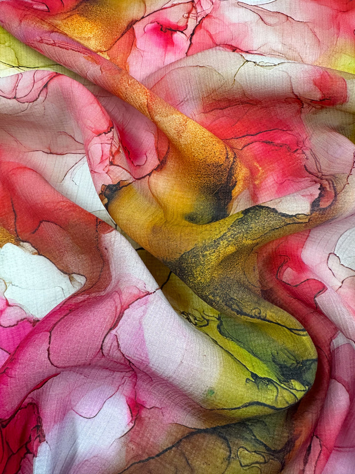 A close-up of crumpled Designer Cotton - Catalina (150cm) from Super Cheap Fabrics showcases vibrant swirls of red, pink, yellow, and green blending seamlessly like a watercolor painting, with intricate patterns creating dynamic movement across this luxury sewing surface.