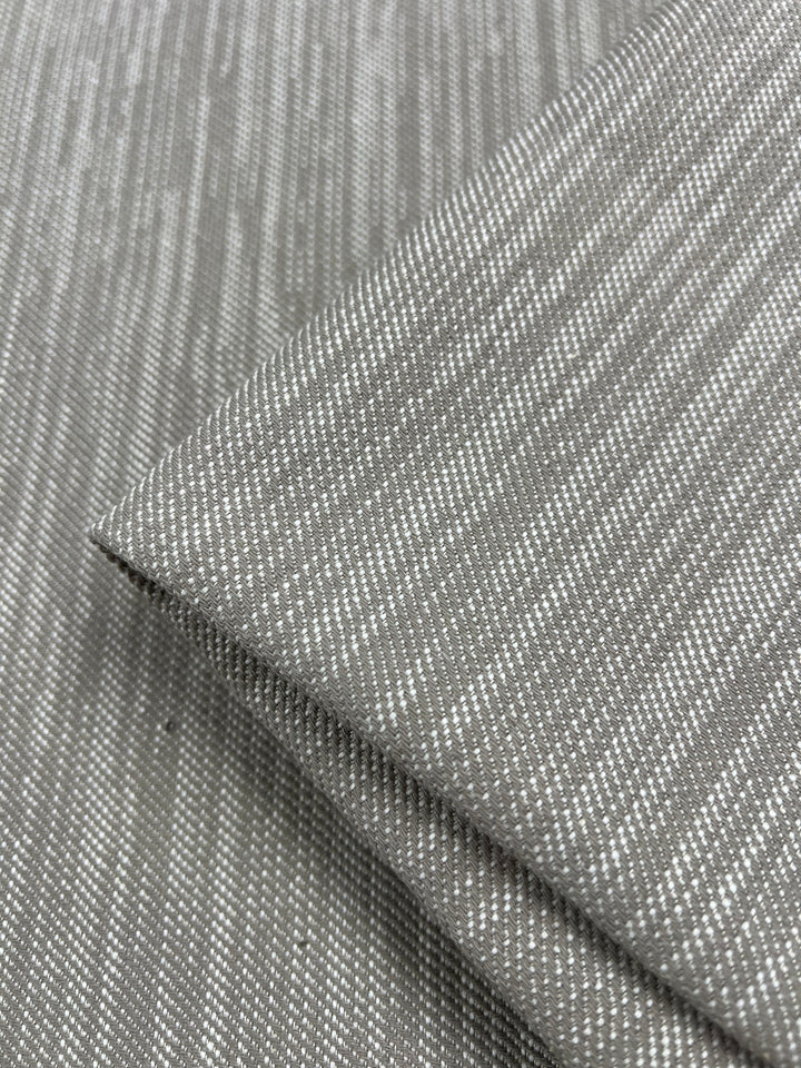Close-up of folded gray Upholstery Twill - Natural - 147cm by Super Cheap Fabrics with a subtle linear pattern. The fabric showcases a texture comprising thin, light-colored lines running diagonally, creating a modern, sleek aesthetic perfect for durable furniture upholstery.