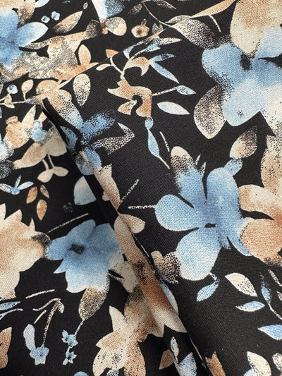 Close-up of Designer Rayon - Dusty Petals (145cm) by Super Cheap Fabrics, featuring lightweight rayon with light blue and beige floral patterns on a black background. Fabric is gently folded to display the design from various angles.