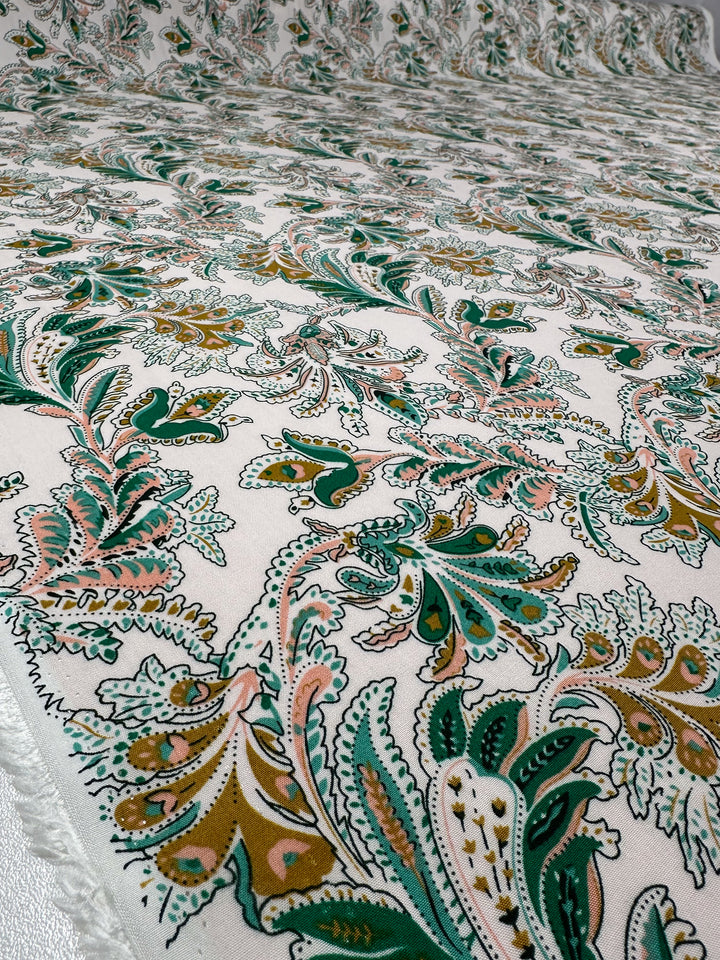 A close-up of Designer Rayon - Verdant Script by Super Cheap Fabrics shows its lightweight 145cm-wide fabric with a vibrant green, gold, and pink floral and paisley print on white, highlighting the intricate design and smooth texture.