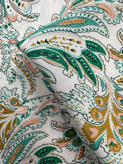 Close-up of Designer Rayon - Verdant Script (145cm) by Super Cheap Fabrics, featuring white fabric with intricate paisley patterns in green, gold, pink, and black, detailed floral and leaf designs, and vibrant prints.
