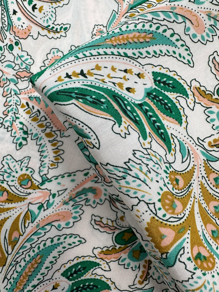 Close-up of Designer Rayon - Verdant Script (145cm) by Super Cheap Fabrics, featuring white fabric with intricate paisley patterns in green, gold, pink, and black, detailed floral and leaf designs, and vibrant prints.