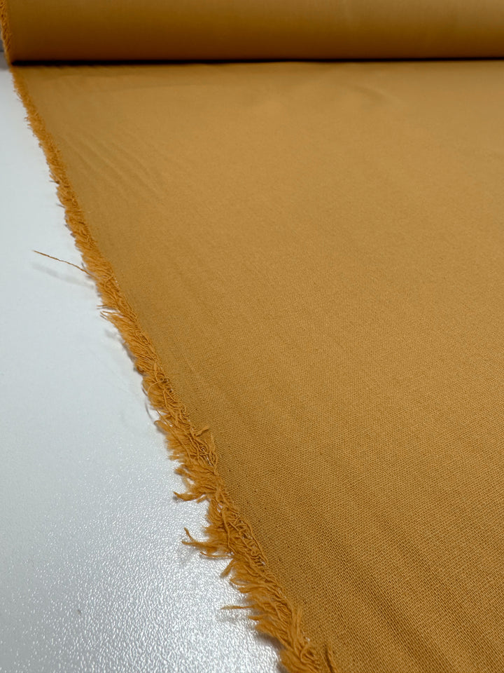 A roll of "Inca Gold" Ramie Linen by Super Cheap Fabrics, 150cm wide, is laid out on a flat surface with frayed edges, creating a rustic look.