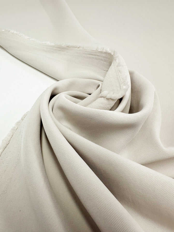 A close-up of Suiting - White Swan - 142cm by Super Cheap Fabrics, featuring light beige polyester fabric with a subtle texture, loosely folded and draped in soft layers, highlighting its unfinished edges.