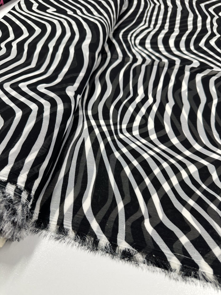 Super Cheap Fabrics' Printed Chiffon - Zebraic - 150cm lies flat, showcasing its black and white wavy stripes. The lightweight polyester fabric's textured edges and curvy patterns create an optical illusion ideal for high fashion garments.