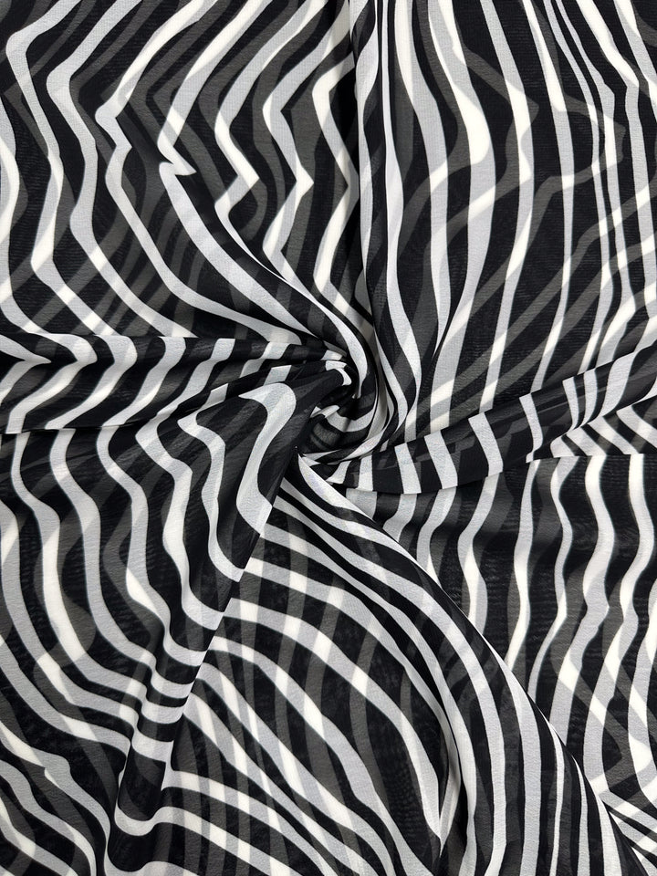 The "Zebraic" Printed Chiffon by Super Cheap Fabrics features an abstract black-and-white pattern with swirling, wavy lines that create an optical illusion reminiscent of zebra stripes. This design on lightweight polyester adds a dynamic, three-dimensional feel, perfect for high fashion statements. Width: 150cm.