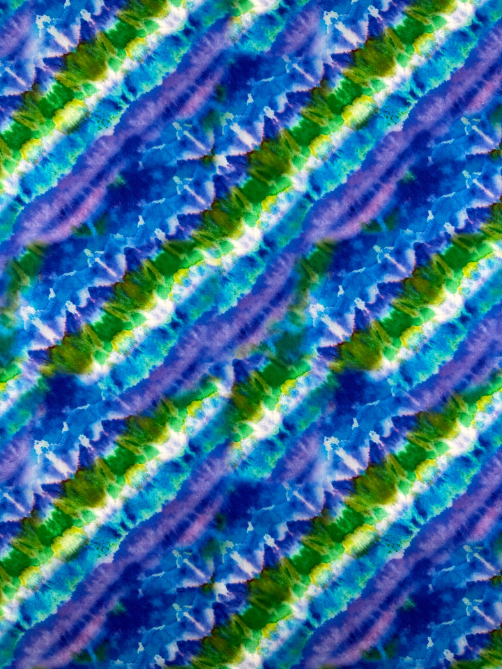 The Printed Cotton - Lizard - 150cm by Super Cheap Fabrics features a vibrant and dynamic abstract pattern with diagonal stripes in shades of blue, green, and purple. This design resembles a watercolor tie-dye effect on lightweight printed cotton fabric, highlighting its textured appearance made from natural cotton fibers.