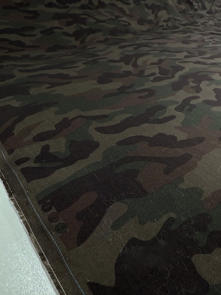 A close-up of Super Cheap Fabrics' Printed Linen - Military - 150cm, featuring a lightweight roll with a green, brown, and black camouflage pattern spread out on a flat surface.