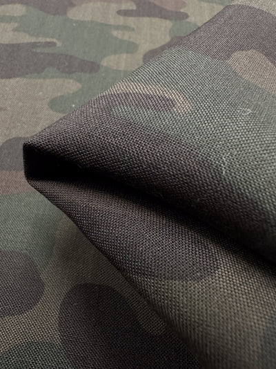 Close-up of Super Cheap Fabrics' Printed Linen - Military - 150cm, showing its green and brown camouflage pattern, visible texture, and weave with part of the fabric folded. Ideal for home decor projects.
