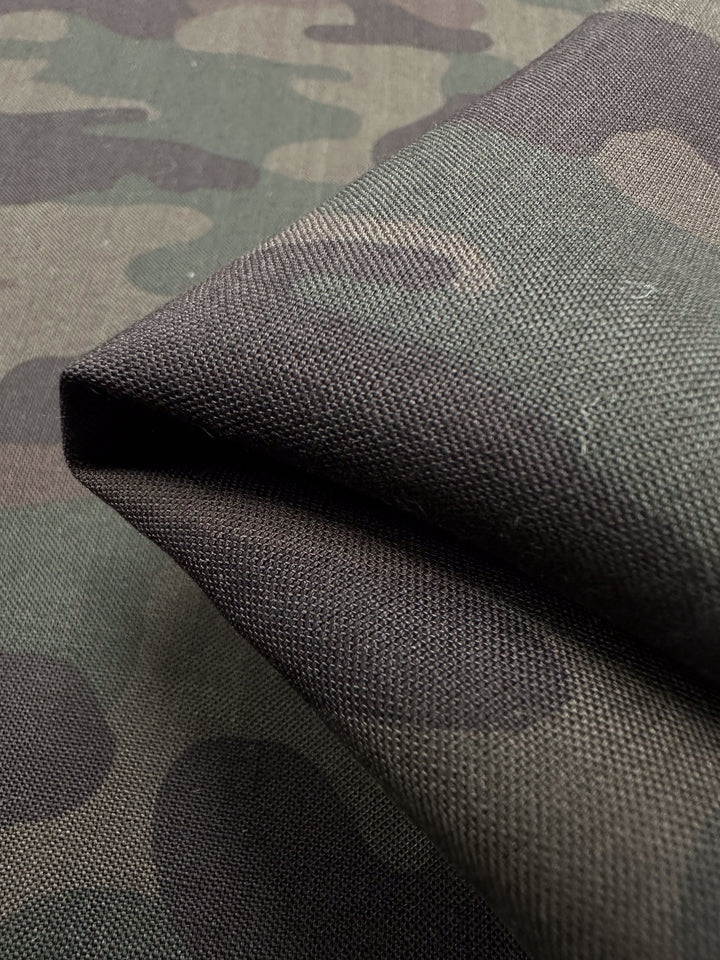 Close-up of Super Cheap Fabrics' Printed Linen - Military - 150cm, showing its green and brown camouflage pattern, visible texture, and weave with part of the fabric folded. Ideal for home decor projects.