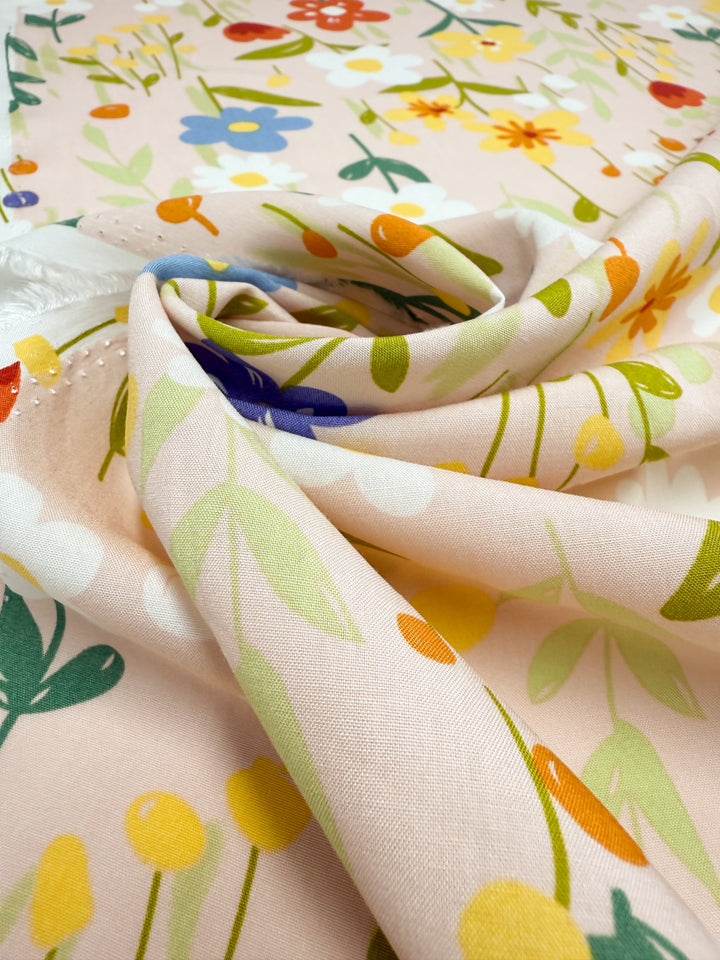 Designer Rayon - Meadow Mingle by Super Cheap Fabrics: soft rayon fabric, 145cm wide, with a colorful floral print in yellow, orange, blue, and green on a pale background—versatile for any creative project.