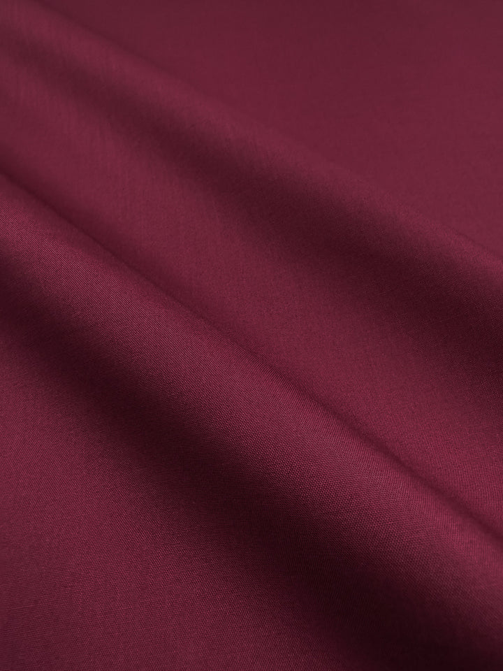 A close-up of Super Cheap Fabrics' Poplin - Mulberry Matte (114cm) highlights its red, lightweight material with a delicate texture and soft finish.
