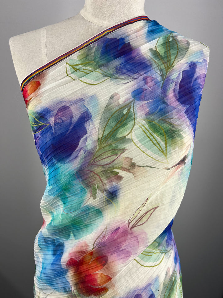 A mannequin showcases Super Cheap Fabrics' Textured Tencel - Dream Flor, a sheer fabric with vibrant floral patterns in blue, purple, red, and green. This 136cm sustainable fabric is pleated with a delicate texture.
