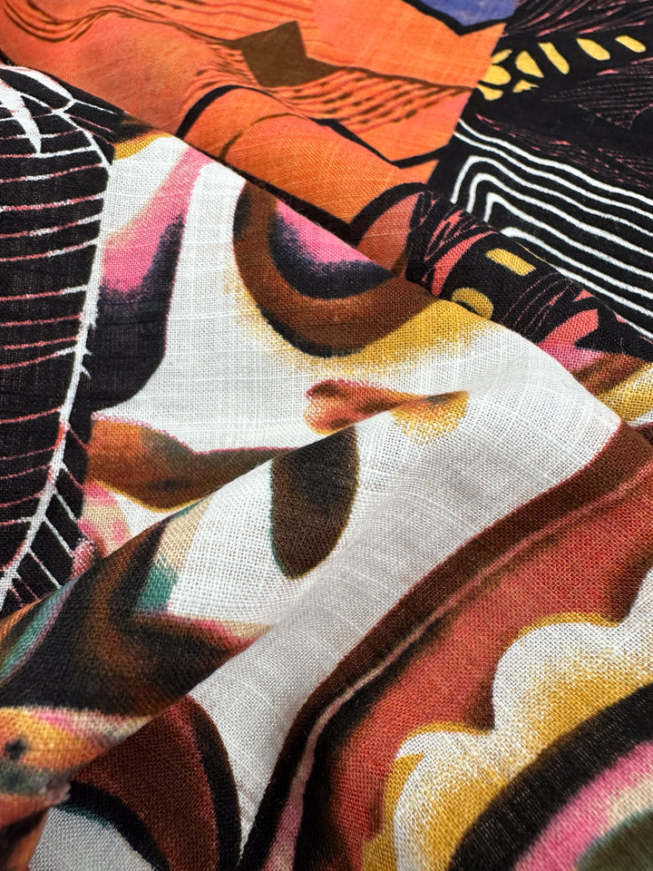 A close-up of "Linen Blend - Patch - 145cm" by Super Cheap Fabrics reveals a lightweight linen fabric with a vibrant abstract pattern in orange, pink, black, and yellow. The visible texture showcases breathable curves and lines creating an intriguing design.