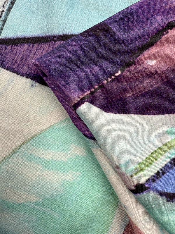 Close-up of Super Cheap Fabrics' Mercerised Rayon - Mid Mod Mirage (150cm), showing breathable, folded fabric with an abstract print in purple, mint green, and white, highlighted by bold brush strokes and soft blended details.