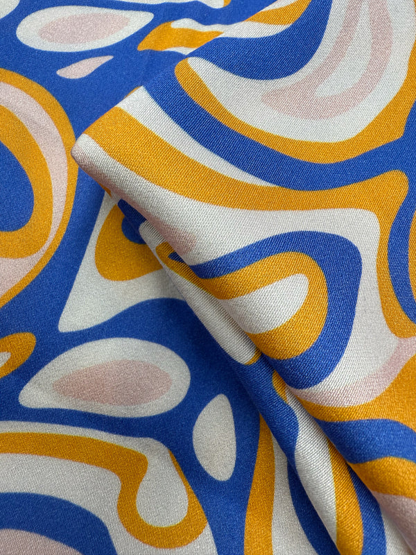 A close-up of Super Cheap Fabrics' Mercerised Rayon - Electric Ember (145cm), showcasing lightweight, breathable rayon with a bold abstract pattern in blue, yellow, pink, and white plus a subtle sheen and fluid drape.
