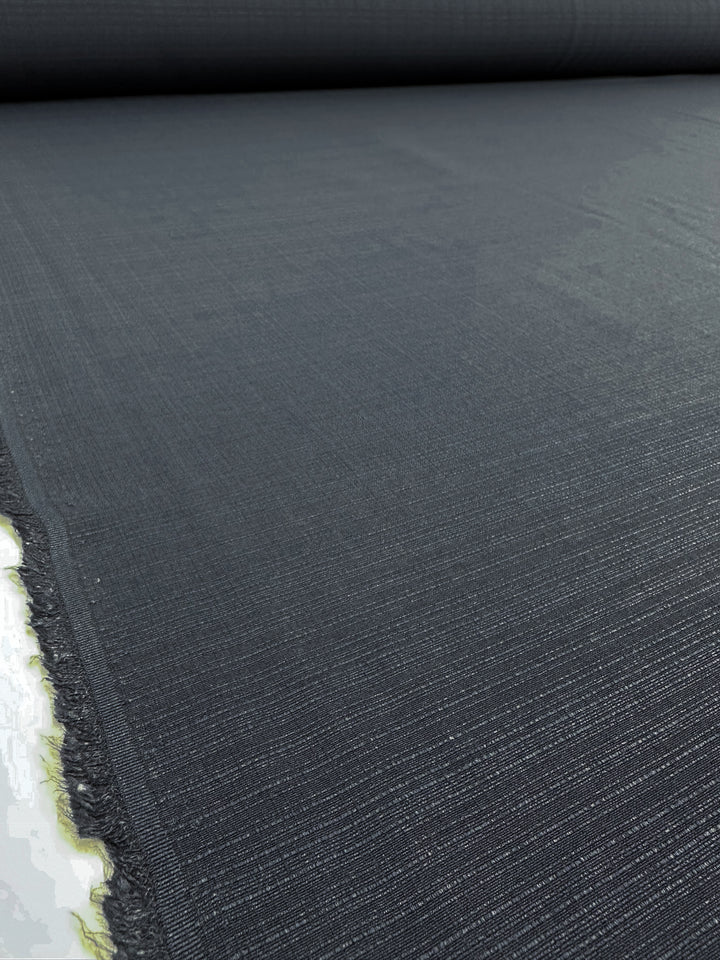 A close-up of the Textured Bengaline fabric in indigo by Super Cheap Fabrics, measuring 145cm in width, highlights its slightly glossy texture. The frayed edges indicate where it was cut, while its turn reveals depth and length.
