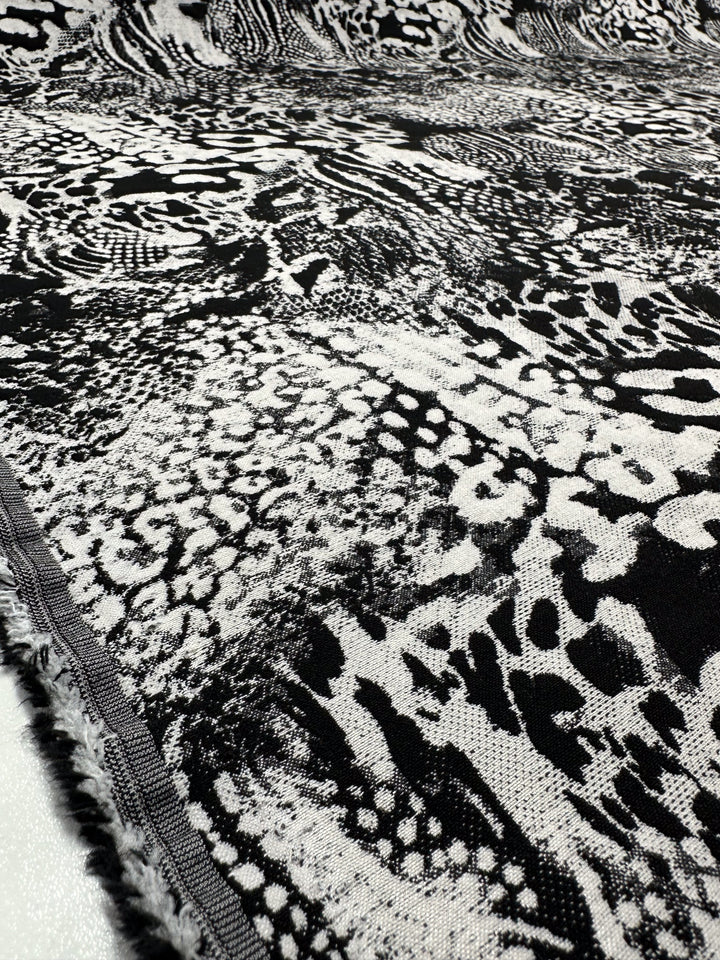 Close-up of intricately woven Jacquard Bengaline - Survivor fabric by Super Cheap Fabrics, featuring a black and white abstract pattern with various textures. This medium-weight, 145cm wide material offers a frayed edge, indicating it is unhemmed.
