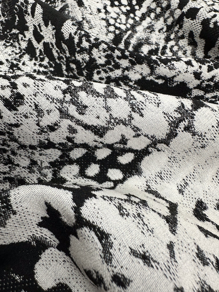Close-up of Survivor Jacquard Bengaline from Super Cheap Fabrics showcases a medium-weight snakeskin-like black and white abstract pattern with textured, intricate shapes and shades. Width: 145cm.