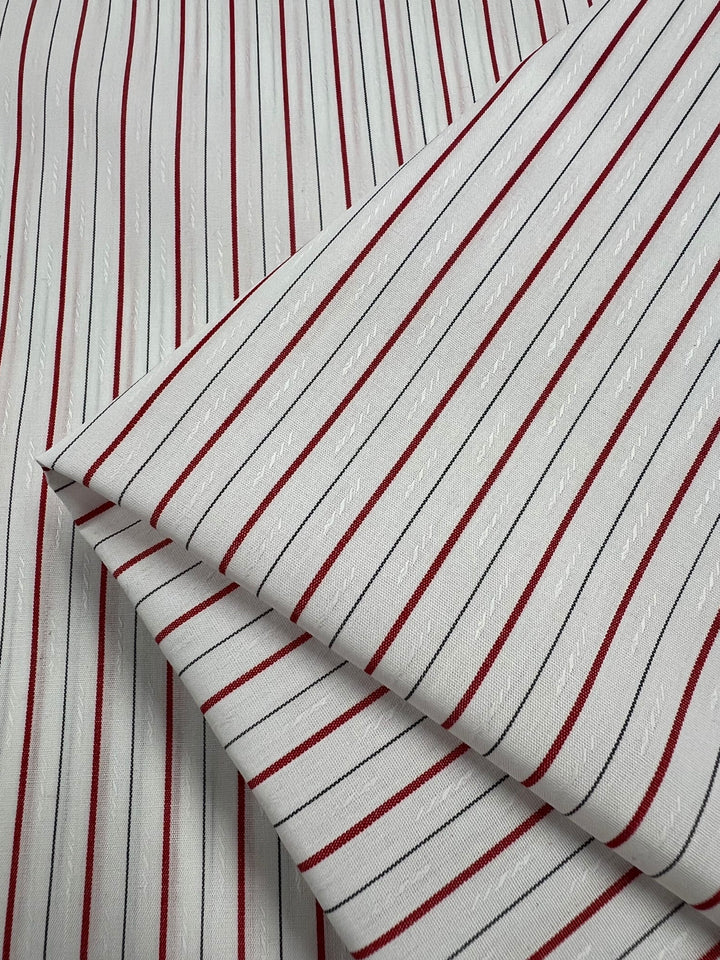 Super Cheap Fabrics’ Shirting - Pins - 145cm is a lightweight white polyester cotton with red and black vertical stripes, subtle woven texture, and neatly folded corners—perfect for versatile projects.