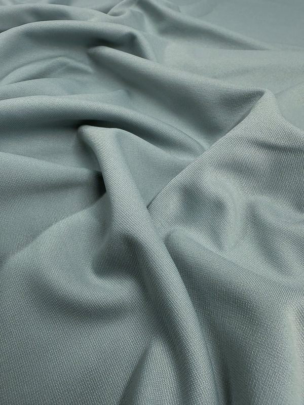 The Ponte - Barely Blue - 155cm from Super Cheap Fabrics is a soft, light teal stretch fabric with a textured surface that drapes smoothly and fluidly, featuring subtle sheen and wrinkle-resistance while creating gentle folds and shadows.