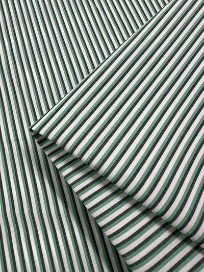 Shirting - Lizard - 150cm by Super Cheap Fabrics features lightweight green and white striped polyester cotton with overlapping diagonal and horizontal folds, ideal for versatile multicolour design projects.