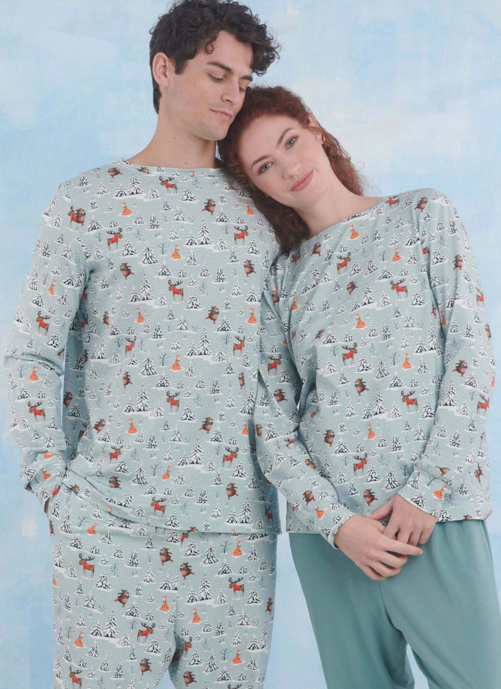 In front of a blue backdrop, a couple showcases the Simplicity S9861 loungewear by Super Cheap Fabrics. Their matching pajamas feature a whimsical winter print with trees and animals. The woman rests her head on the man's shoulder, both smiling warmly, encapsulating comfort and style.