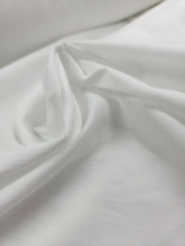 A close-up of Super Cheap Fabrics' Poplin - Tex White - 147cm shows a smooth poly/cotton fabric with gentle folds and a soft sheen. This lightweight material is ideal for childrenswear, providing comfort and slight translucency.