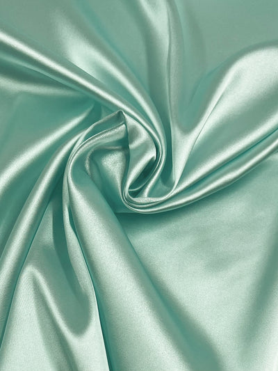 A close-up of Satin Deluxe - Mint by Super Cheap Fabrics, a smooth, shiny 150cm-wide dressmaking fabric with soft folds and swirling patterns in lightweight polyester.
