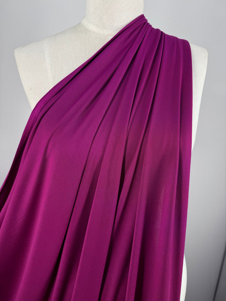 A mannequin is elegantly draped with the Festival Fuschia Cotton Lycra from Super Cheap Fabrics, showcasing its soft texture and slight sheen in pleats over one shoulder.