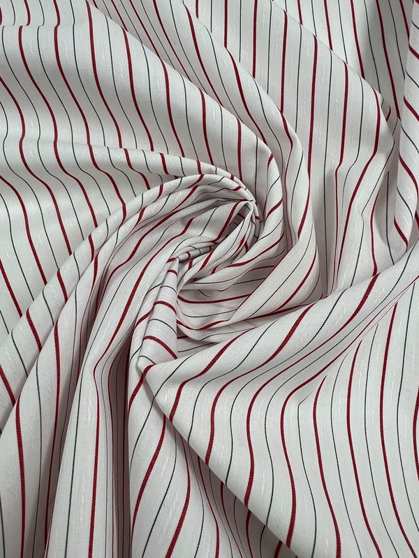 Shirting - Pins - 145cm by Super Cheap Fabrics is a white polyester cotton fabric with thin red vertical stripes. Lightweight and versatile, it features dynamic folds in a swirling, gathered pattern that highlights its flow and texture.