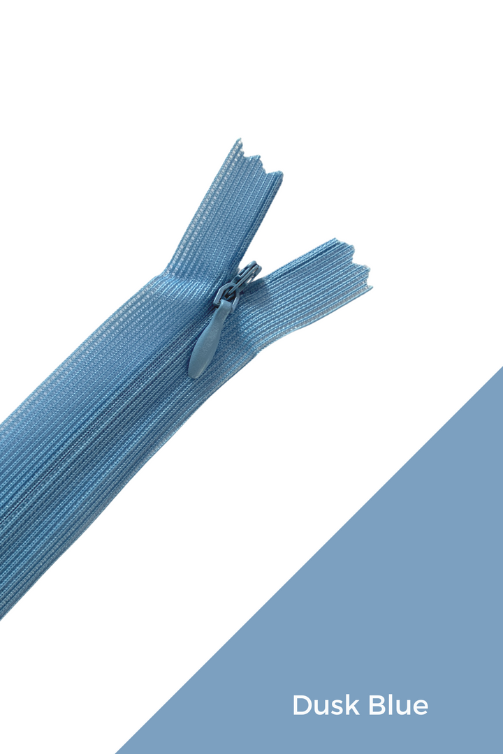 A close-up of the Super Cheap Fabrics Invisible Zip - 30cm - Blues in dusk blue, partially zipped, placed on a white background with a diagonal dusk blue section in the bottom right corner. The text "Dusk Blue" is written in the blue section, showcasing an elegant finish.