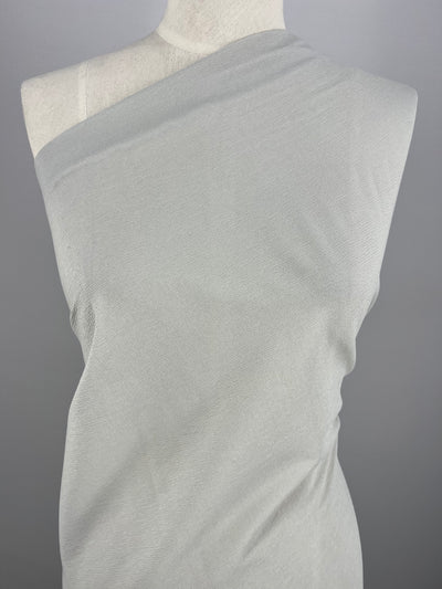A dress form displays Super Cheap Fabrics' Stretch Crinkle - Mirage Gray - 140cm, a medium-weight polyester, draped one-shoulder style against a neutral gray background.