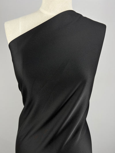 A one-shoulder black dress draped on a mannequin against a plain white background. The medium weight Crepe De Chine - Black - 150cm fabric from Super Cheap Fabrics appears smooth and slightly shiny, creating elegant folds that enhance the dress's sleek and sophisticated look.