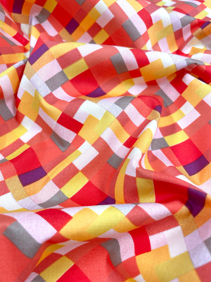 A close-up of Super Cheap Fabrics' Printed Poplin - Jigsaw (112cm) reveals a vibrant, crumpled fabric with geometric squares in red, orange, yellow, white, and gray. Its intersecting lines form an energetic design ideal for creating breathable clothing.